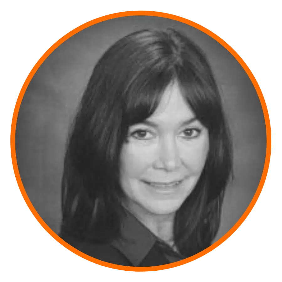A black and white portrait of a woman with long dark hair, smiling slightly. She is wearing a dark top. The image is enclosed in an orange circular border.