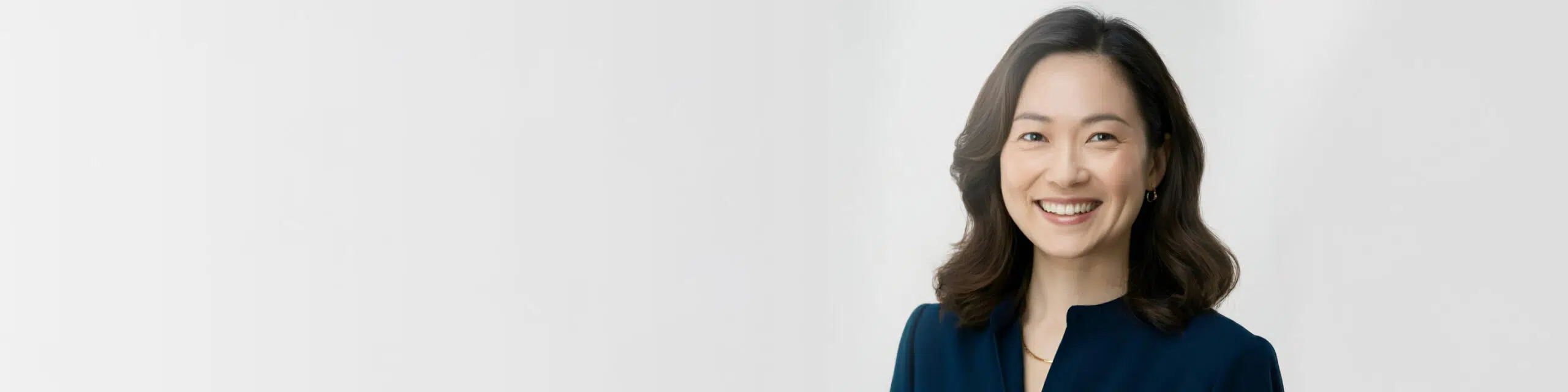 Smiling woman with shoulder-length dark hair wearing a dark blue blouse against a light gray background.